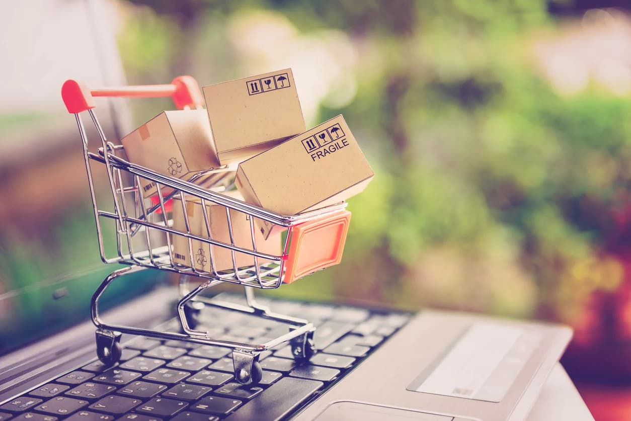 A toy shopping cart with boxes in it, sitting on top of a laptop.